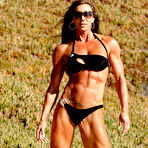 Pic of Bodybuilder Lynnie Brooks poses on sandy ground in a bikini and sunglasses