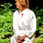 Pic of Older redhead removes a robe to stand naked in red heels while in the woods